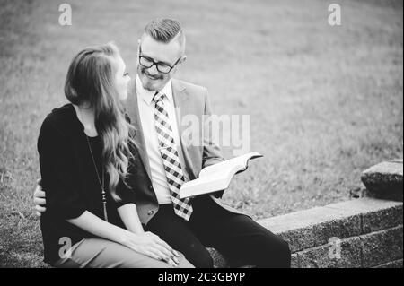 Scala di grigi di una coppia seduta su blocchi e amorevolmente leggere un libro Foto Stock