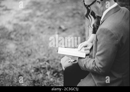 Vista dall'alto in scala di grigi di una coppia seduta in un giardino e leggendo con amore un libro insieme Foto Stock