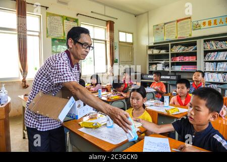 (200620) -- WUXUAN, 20 giugno 2020 (Xinhua) -- Wei Xuxi consegna il latte in scatola agli studenti della scuola primaria di Shuanggui nella città di Ertang della contea di Wuxuan, regione autonoma di Guangxi Zhuang, 19 giugno 2020. Wei Xuxi, insegnante di 57 anni della città di Ertang nella contea di Wuxuan, ha trascorso oltre 30 anni a insegnare in campagna dopo essersi laureato alla scuola superiore nel 1985. Ci sono 32 studenti in due classi nella scuola elementare di Shuanggui, una scuola su piccola scala dove lavora Wei. Invece di edifici fatiscenti, o tavoli e sedie rotti, multimedia e molte altre attrezzature di insegnamento avanzate fare Foto Stock