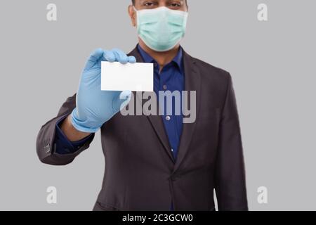 Uomo d'affari che mostra la scheda di visita che indossa maschera medica e guanti primo piano isolato. Indiane uomo di affari carta bianca in mano Foto Stock