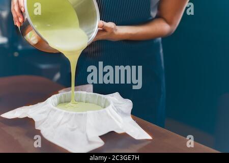 Donna che versa l'impasto di tè verde matcha in una muffa imbottita con carta pergamena. Foto Stock