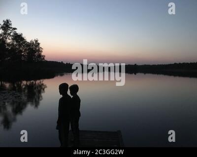 Persone che si levano in piedi sul lago durante un tramonto Foto Stock