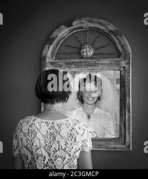 Donna anziana che guarda nello specchio al riflesso più giovane come una sposa Foto Stock