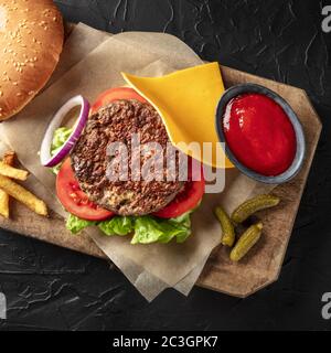 Hamburger con manzo, formaggio, cipolla, pomodoro e insalata verde, con un panino e ketchup, pallini quadrati sopra uno sfondo nero Foto Stock