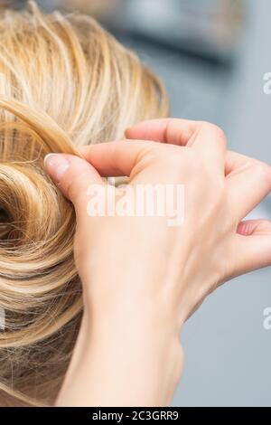 Primo piano vista posteriore del parrucchiere che fa acconciatura per capelli lunghi di donna bionda. Foto Stock