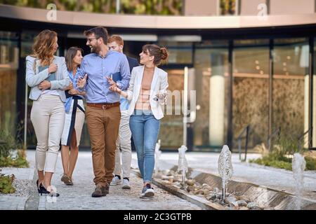 gruppo di colleghi che camminano, parlano, ridono, di fronte al business building Foto Stock