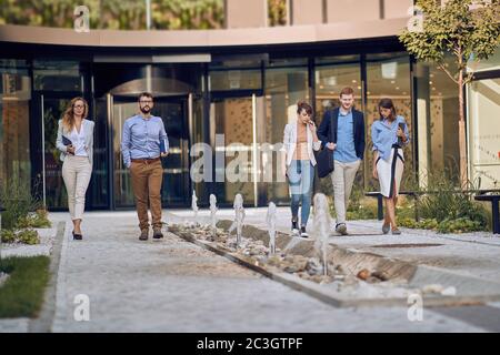 gruppo di uomini d'affari caucasici che camminano e parlano di fronte all'edificio degli affari Foto Stock