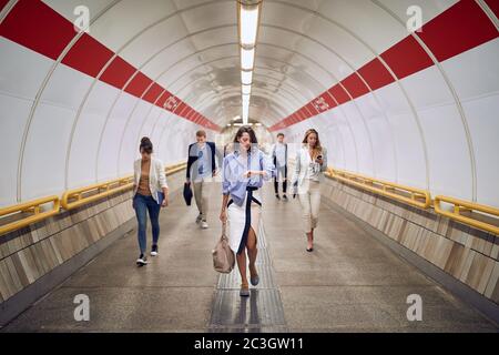 gruppo di persone caucasiche che camminano attraverso il tunnel sotterraneo pedonale, controllando il tempo, guardando l'orologio da polso, il telefono cellulare Foto Stock