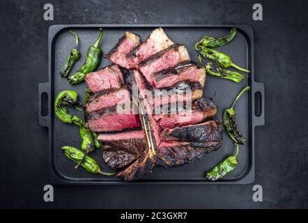 Barbecue secco wagyu invecchiato porterhouse bistecca di manzo affettato con grande filetto pezzo con peperoncino caldo come vista dall'alto su un blac design moderno Foto Stock