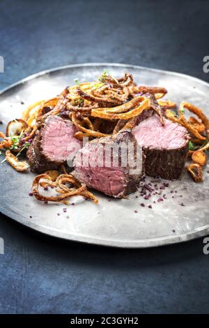 Filetto di manzo stagionato tradizionale con anelli di cipolla fritti e patate serviti come closeup su una piastra dal design moderno Foto Stock