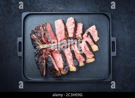 Barbecue secco wagyu invecchiato porterhouse bistecca di manzo affettato con grande pezzo di filetto come vista dall'alto su un moderno design nero ghisa tra Foto Stock