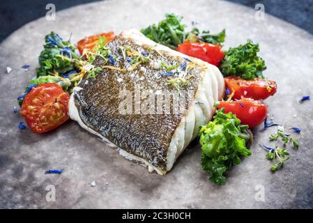 Filetto di merluzzo europeo fritto gourmet skrei con kalette e pomodori come primo piano su un piatto dal design moderno Foto Stock