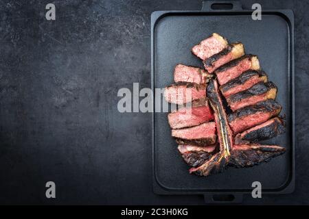 Barbecue secco wagyu invecchiato porterhouse bistecca di manzo affettato con grande pezzo di filetto come vista dall'alto su un moderno design nero ghisa tra Foto Stock
