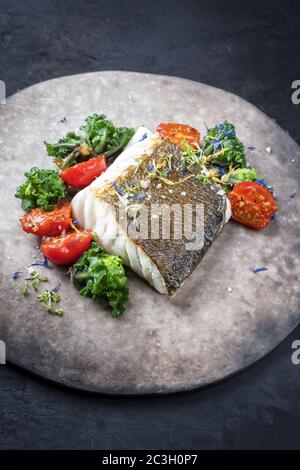 Filetto di merluzzo europeo fritto gourmet skrei con kalette e pomodori come primo piano su un piatto dal design moderno Foto Stock