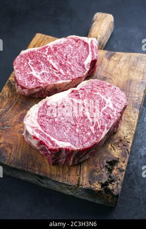 Il wagyu crudo invecchiato ha fatto un'entrecote di manzo arrosto come closeup su un rustico tagliere di legno Foto Stock