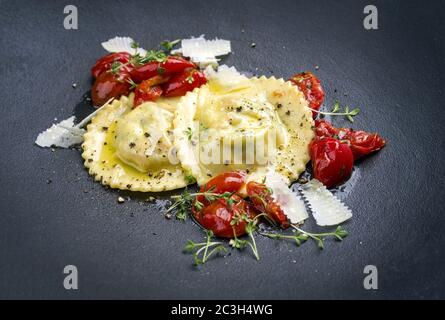 Tradizionale pasta di ravioli italiana con parmigiano e pomodori fritti come primo piano su un piatto dal design moderno Foto Stock