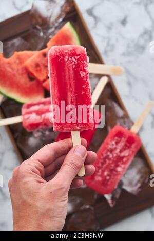 Servizio di una festa estiva. Sorbetto rosso congelato con il gusto di anguria giace su grandi pezzi di ghiaccio con pezzi di anguria matura Foto Stock