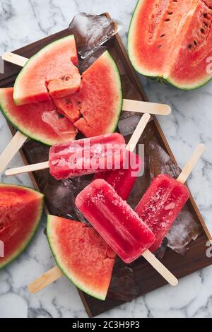 Servizio di una festa estiva. Sorbetto rosso congelato con il gusto di anguria giace su grandi pezzi di ghiaccio con pezzi di anguria matura Foto Stock