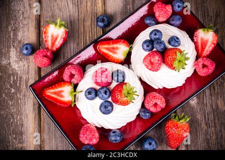 Piatto di frutta estivo composto da fragole, lamponi e mirtilli su nidi pavlova meringa Foto Stock