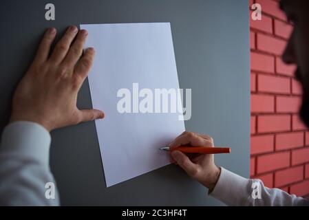 un uomo scrive su un foglio bianco di carta su uno sfondo grigio Foto Stock