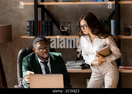 Attraente uomo d'affari africano con giovane donna d'affari che lavora su computer portatile in ufficio Foto Stock