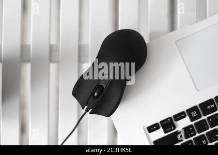 Un primo piano di un mouse nero su un computer portatile bianco e sfondo bianco del tavolo Foto Stock