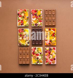 Cioccolato di vari colori e ripieni colorati con fette di frutta a guscio su fondo marrone. Layout piatto della vista dall'alto. Foto Stock