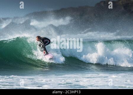 Spettacolare azione di surf come una giovane donna surfer cavalca un wave a Fistral a Newquay in Cornovaglia. Foto Stock