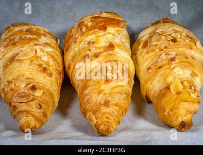 Tre deliziosi croissant dorati, ricoperti di mandorle in fiocchi e cotti con un ripieno di mandorle dolci, su carta a prova di grasso calda al forno. Foto Stock