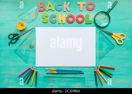 Concetto di ritorno a scuola. Posa piatta di sfondo turchese in legno con testo di lettere colorate, bianco, forniture scolastiche, e foglie secche d'autunno. Centro benessere copie Foto Stock