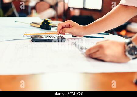 progettazione utilizzando la calcolatrice per la contabilità e l'analisi della struttura degli edifici da blueprint. Foto Stock