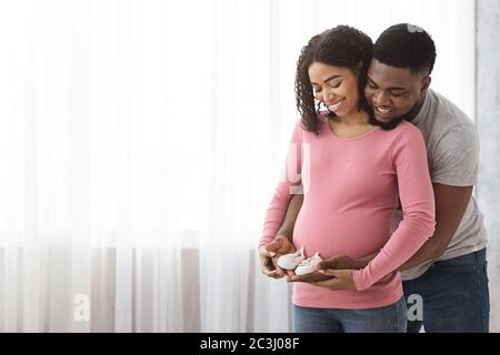 Carino nero che si aspetta famiglia che tiene scarpe per bambini Foto Stock