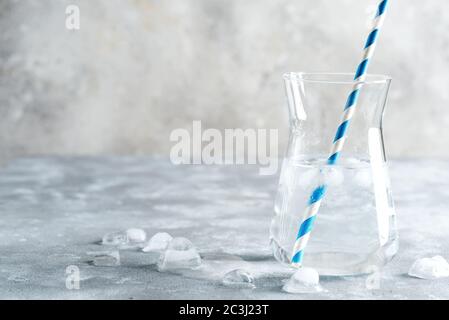 Rinfrescanti acqua fredda naturale limpida in un vaso di vetro con cubetti di ghiaccio con paglia di plastica su un tavolo grigio marmo, spazio copia. Freddo estate drin non alcolico Foto Stock