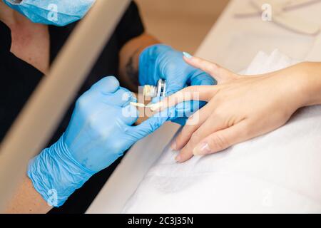 Primo piano di Beautician dipingendo i chiodi del suo cliente in vernice blu e gialla. Foto Stock