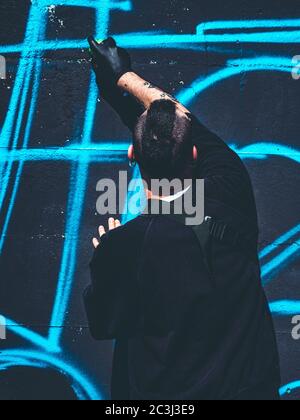 Scatto verticale di un giovane maschio che fa un graffiti sopra una parete nera Foto Stock