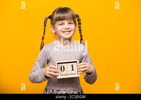 Primo piano ritratto di prima ragazza grader con spirali divertenti guardando la fotocamera e tenere in legno calendario fissato il 1 settembre isolato su luminoso YE Foto Stock