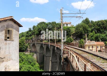 I binari ferroviari passano su un ponte di pietra attraverso un paesaggio ricco di vegetazione e alberi. Rotaia rialzata in prospettiva. Archi in pietra. Foto Stock