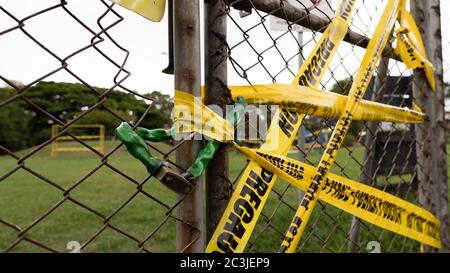 Applicare un nastro di precauzione giallo su una catena arrugginita recinzione in un parco sotto un cielo nuvoloso Foto Stock
