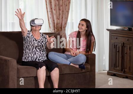Donna anziana con cuffie per realtà virtuale o occhiali 3d che si diverte con la nipote. Persone che si divertono con il nuovo concetto di tecnologia. Focus su sen Foto Stock