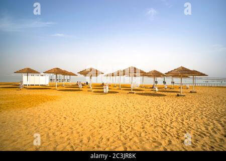 Bella spiaggia con sedie a sdraio e ombrelloni con tetto di paglia nella località di Ein Bokek Israele. Foto Stock