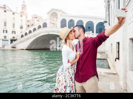 Una romantica coppia innamorata in vacanza a Venezia. I giovani si baciano e prendono un selfie di fronte al Ponte di Rialto. Foto Stock