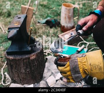 Inquadratura ad alta angolazione di una persona che indossa guanti di sicurezza mentre lavorare con ferro fuso in una foresta Foto Stock