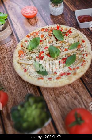 Colpo verticale di una pizza di pollo circondata da spezie una superficie di legno Foto Stock