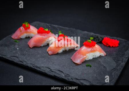 Sushi perfetto, cucina tradizionale giapponese. Delizioso kiguiri di tonno con capriolo (caviale) sulla piastra decorata, fondo nero. Foto Stock