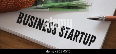 Copybook con testo di avvio di Business scritto su circa 100 banconote in euro sul tavolo. Crowdfunding funddraising donazione basata nuovo concetto di business Foto Stock