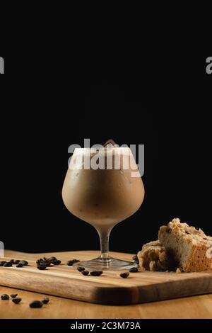 Primo piano di un bicchiere di cappuccino di ghiaccio su un legno piatto con decorazioni su fondo nero Foto Stock