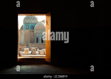 Porta aperta nella stanza buia che conduce alla necropoli Shah-i-Zinda, un cimitero del complesso commemorativo a Samarkand, Uzbekistan Foto Stock