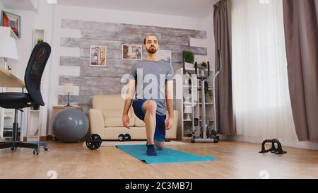 Fit uomo allenando le gambe facendo avanti si affondo sul tappeto yoga a casa. Foto Stock