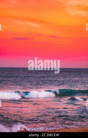 Colpo mozzafiato delle onde dell'oceano che si illuminano sotto il cielo rosso - ottimo per gli sfondi Foto Stock