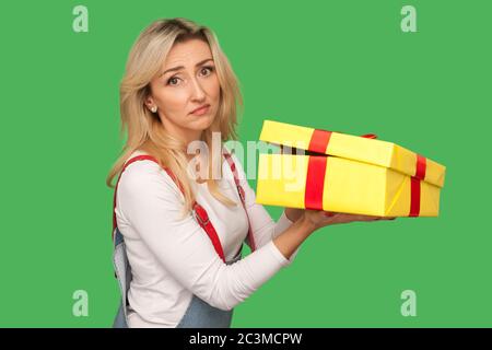 Ritratto di donna adulta dispiaciuta sconvolto in tute in denim che tengono il regalo non imballato, disimballando presente e guardando con deluso espressione triste. ind Foto Stock